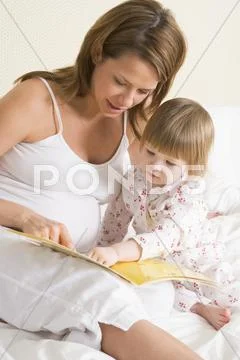 Pregnant woman in bedroom reading book with daughter Stock-Fotos