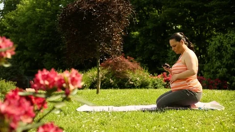 Pregnant woman checking smartphone while sitting in the garden and receives good Stock Footage 76184471