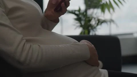 Pregnant Woman Checking Smartphone While Sitting Indoors Near Window Видео 336522583