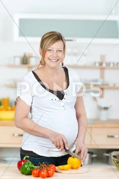 Pregnant woman cutting yellow paprika at kitchen counter Stock Photos