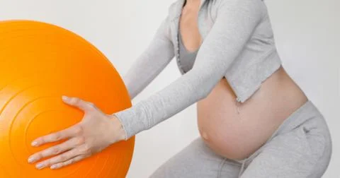 Pregnant woman exercising with fit ball making squats Stock Photos