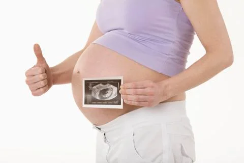 Pregnant woman holding sonogram image, showing thumbs up sign, mid section Stock Photos