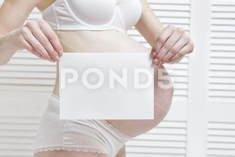 Pregnant woman is holding a white blank sheet. Belly on the back Stock Photos