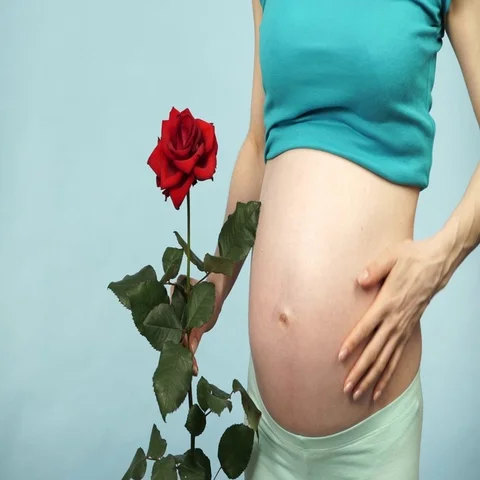 Pregnant woman holds rose flower and caressing her belly 4K Stock Footage