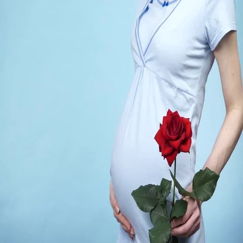 Pregnant woman holds rose flower and caressing her belly 4K Stock Footage