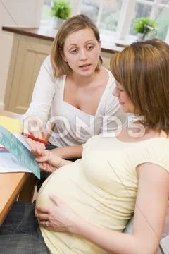 Pregnant woman in kitchen with friend reading pamphlet Stock-Fotos