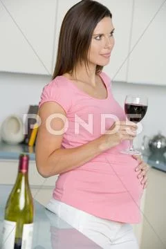 Pregnant woman in kitchen with glass of red wine Stock-Fotos