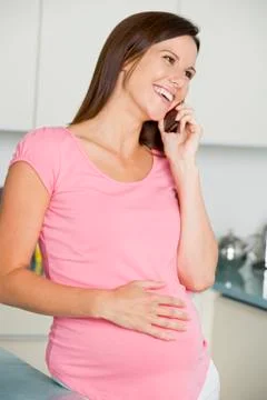 Pregnant woman in kitchen talking on cellular phone and smiling Stock Photos
