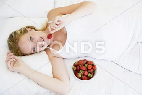 Pregnant woman lying in bed with bowl of strawberries smiling Stock-Fotos