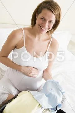 Pregnant woman packing baby clothing in suitcase smiling Stock Photos