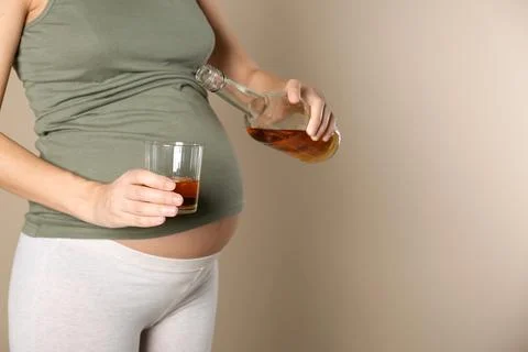 Pregnant woman pouring whiskey into glass on color background. Alcohol addict Stock Photos