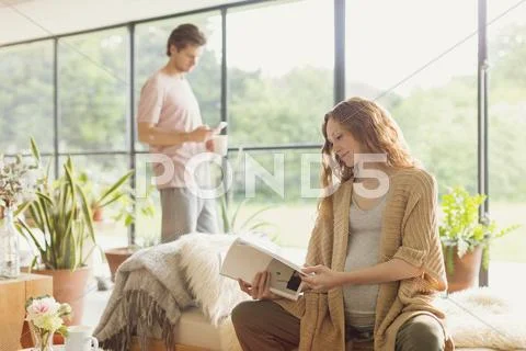 Pregnant woman reading book in living room Stock Photos