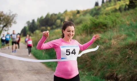 Pregnant woman runner crossing finish line in a race competition in nature. Stock Photos