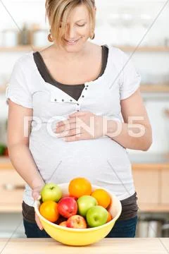 Pregnant woman showing fruitbowl at kitchen counter Stock Photos