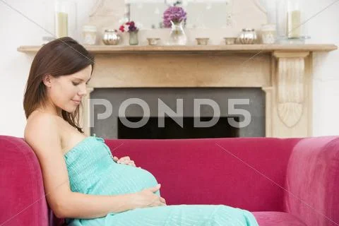 Pregnant woman sitting in living room smiling Stock Photos