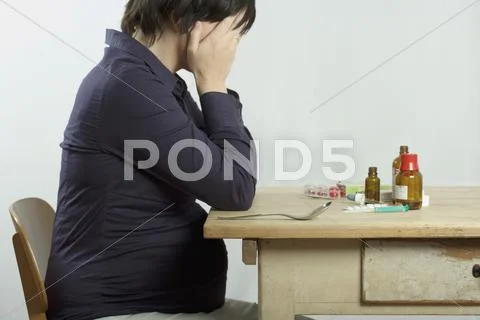 A pregnant woman sitting at a table filled with drugs Stock Photos