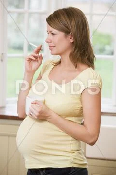 Pregnant woman standing in kitchen with coffee and cigarette Stock-Fotos