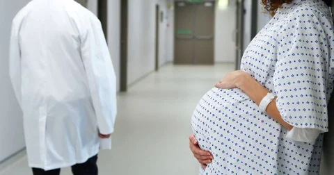 Pregnant woman touching her belly while doctor walking in corridor Stock Footage