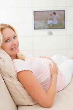 Pregnant woman watching television smiling Stock Photos