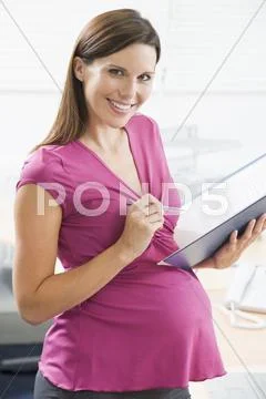 Pregnant woman at work writing in binder smiling Stock-Fotos