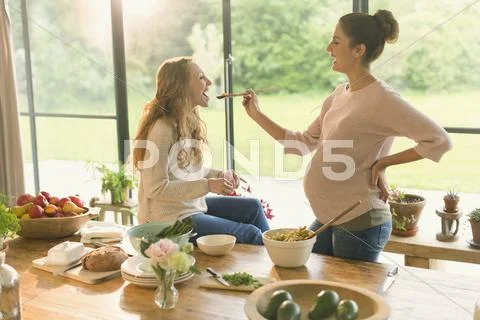 Pregnant women cooking and tasting food at table Stock Photos