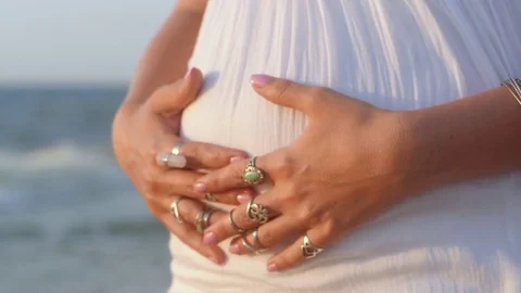 Pregnant young gypsy woman with Boho jewelry touching her belly. Girl in white Stock Footage