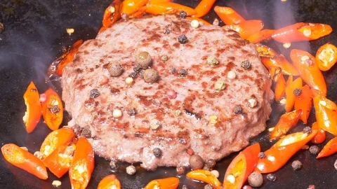 Premium beef burger is being fried with hot red peppers in UHD Video stock 100533052