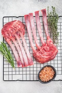 Premium raw lamb rack bone in meat on cooling rack with herbs light stone b.. Stock Photos