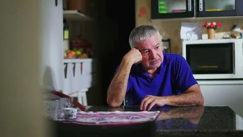 Preoccupied senior man at kitchen table ruminating problems, candid domesti.. Stock Photos