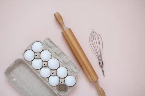 Preparation for baking. Cassette of eggs, rolling pin and whisk on a light Stock Photos