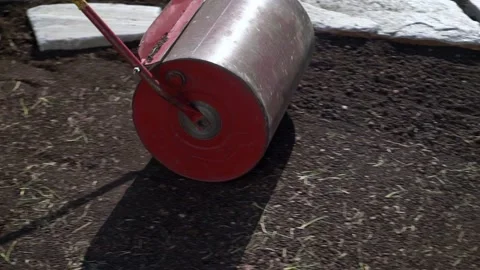 Preparation of turf for flooring, man rolling heavy iron barrel for better co Stock Footage 208362698