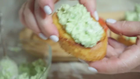 To prepare the appetizer, spread the avocado sauce on the croutons. Stock Footage 254472457