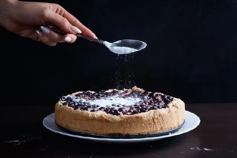 Prepared berry pie on the table in the kitchen the cook sprinkles powder from a Stock Photos