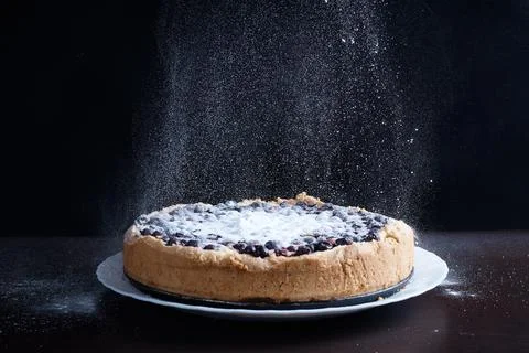 Prepared berry pie on the table in the kitchen the cook sprinkles powder from a Stock Photos