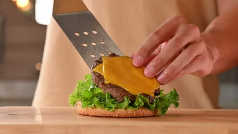 Preparing and assembling a burger. The cook places a burger meat patty on a bun Stock Footage 296071273