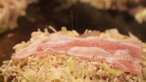 Preparing Authentic Hiroshima-style Okonomiyaki with Cabbage and Pork Belly on T Stockbeeldmateriaal 333600291