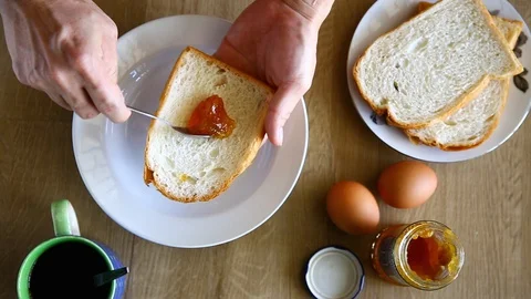 Preparing breakfast at home, spreading jam on bread slices Stock Footage 129176338