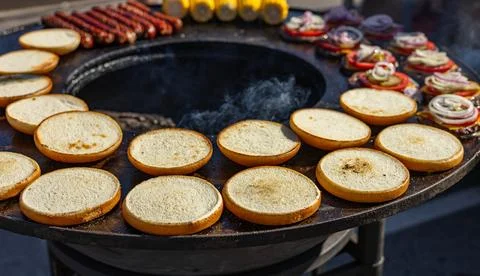 Preparing burger buns. The buns are arranged in a circle on a hot flat-top gr Stock Photos