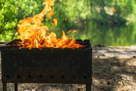 Preparing charcoal grill with open flame for outdoor barbecue near lake Stock-Fotos