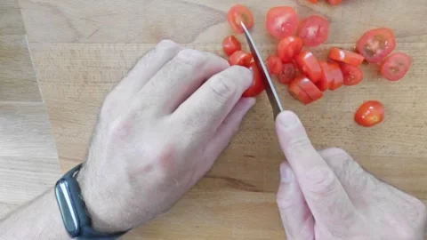 Preparing cherry tomatoes by slicing them on a wooden board. Male hands wit.. Video stock 282710987