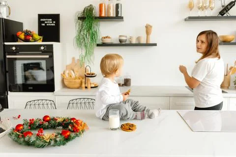 Preparing for Christmas. Mom is working in the kitchen while her son sits and 库存照片