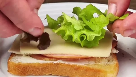 Preparing a delicious sandwich with ham cheese and lettuce on toasted bread Stock Footage 324943448