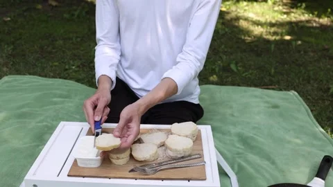 Preparing a delicious spread using fresh bread outdoors during a sunny day Stock Footage 297365769
