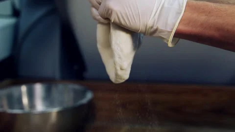 Preparing dough for baking pizza. Chef's hands in gloves pass a piece of dough Stock Footage 318310469