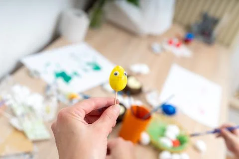 Preparing for Easter person holds painted yellow egg with googly eyes on a .. Stock Photos