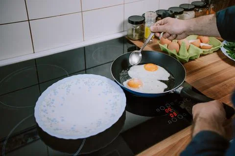 Preparing eggs for breakfast. Overhead view of black kitchen stove  Stock Photos