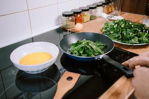 Preparing eggs with spinach for breakfast. Overhead view of black kitchen Stock Photos