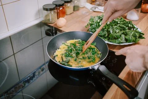 Preparing eggs with spinach for breakfast. Overhead view of black kitchen  Stock Photos