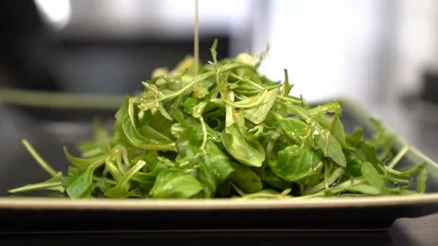 Preparing fresh arugula salad by pouring olive oil dressing on a dark plate Stock Footage 337899787