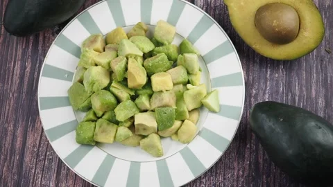 Preparing fresh avocado pieces on a plate with whole avocados nearby Stock Footage 345624506
